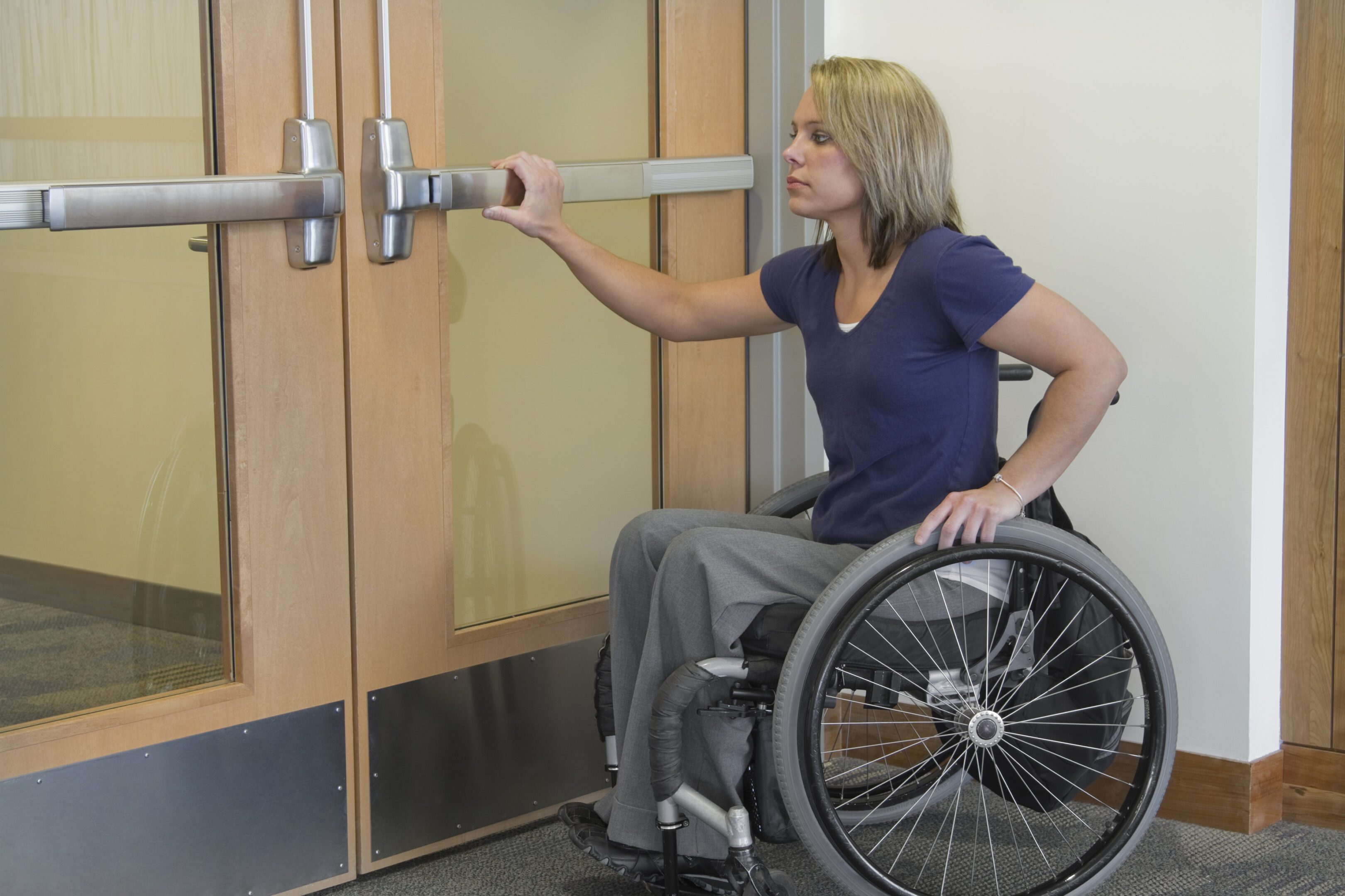 Woman in wheelchair reaching to open doors